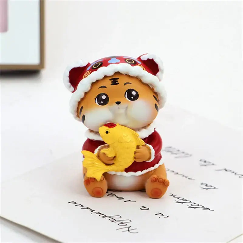 Cute orange lucky tiger figurine wearing a red and white santa hat holding a yellow fish miniature home decor