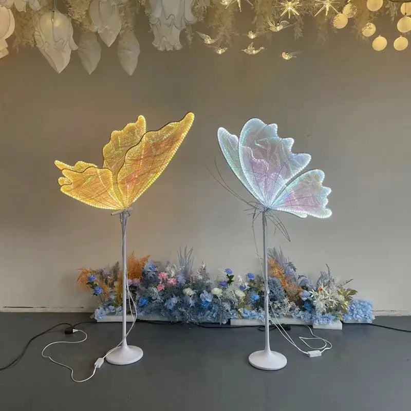 Two decorbites luminescent butterfly floor lamps glowing warm yellow and soft iridescent blue for wedding party decor