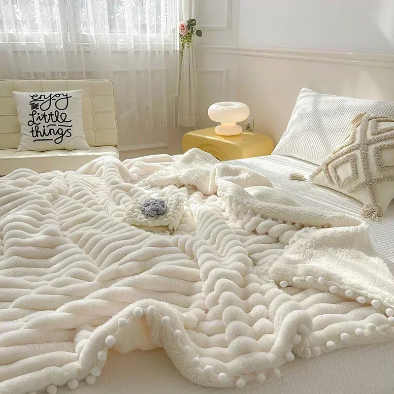 Cream-colored fluffy blanket with pom-poms, likely made of plush material.
