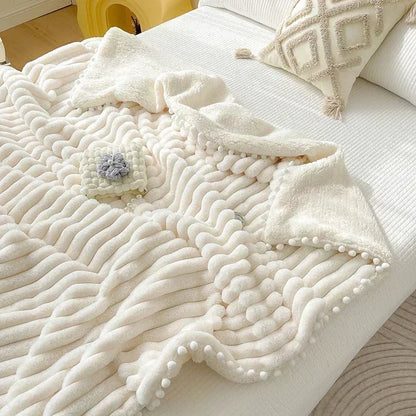Cream-colored textured throw blanket with white pom-poms and a diamond pattern.