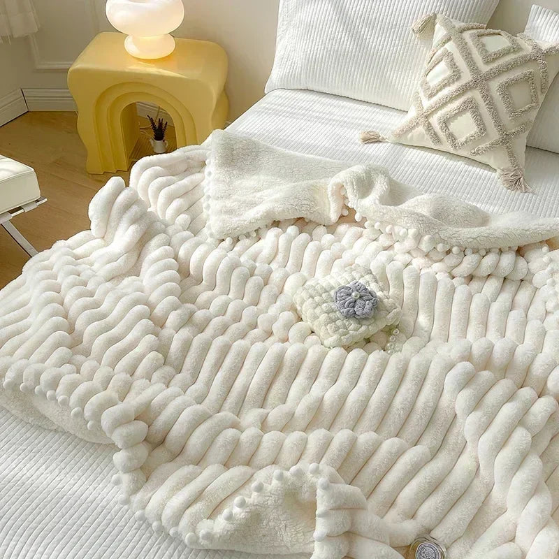 Cream-colored chenille throw blanket with textured wave pattern and pom-pom trim.