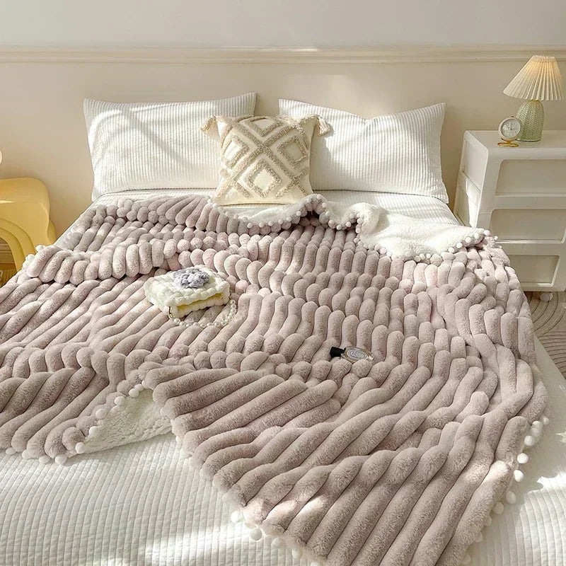 Beige fluffy blanket with pom-poms and wave pattern, likely from a luxury bedding brand.