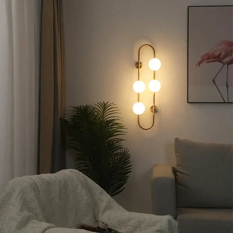 Modern gold-toned decorbites luxe glass ball wall sconce with four glowing bulbs for bedroom and living room use