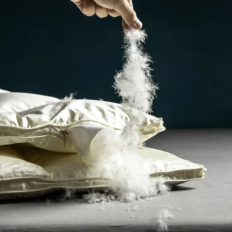 A hand pulls fluffy white down feathers from a cream decorbites luxe goose duck satin pillow for cozy warmth