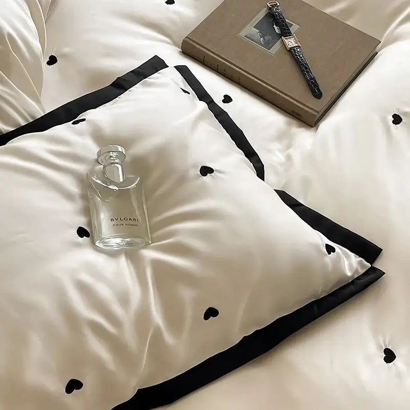 A clear glass bottle of Bvlgari pour homme perfume on an ivory satin pillow with luxe heart embroidered bedding set