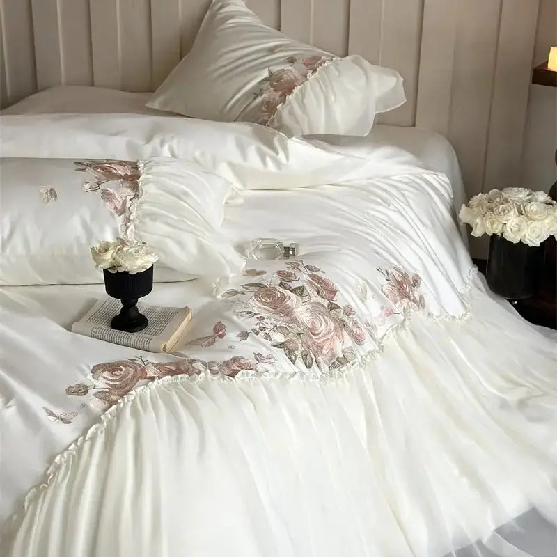 Elegant white satin bedding set with delicate pink and beige rose embroidery and ruffled edges from DecorBites Luxe Lace Ruffles