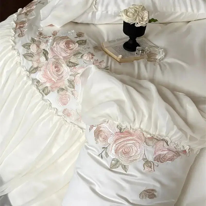 White satin bedding set with delicate pink and beige rose embroidery and ruffled edges from DecorBites Luxe Lace Ruffles