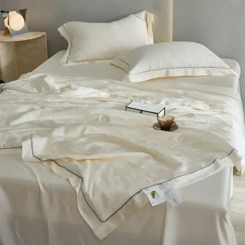 Cream-colored cream-colored satin summer blanket with subtle texture and dark gray piping from decorbites luxe lyocell with mulberry silk fill
