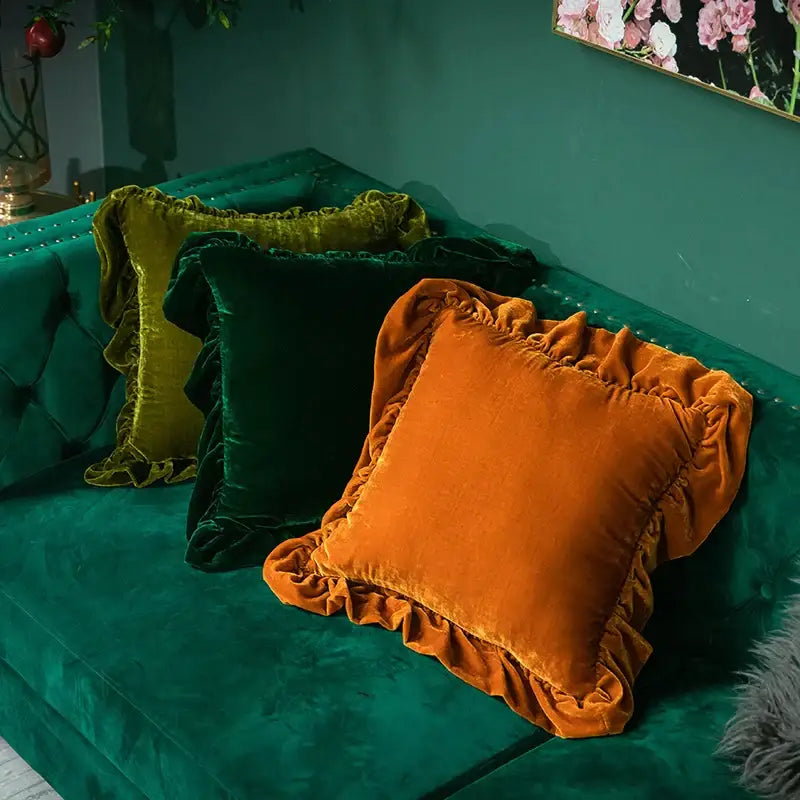 Three velvet euro pillow shams in mustard yellow burnt orange and deep green with ruffled edges on emerald sofa