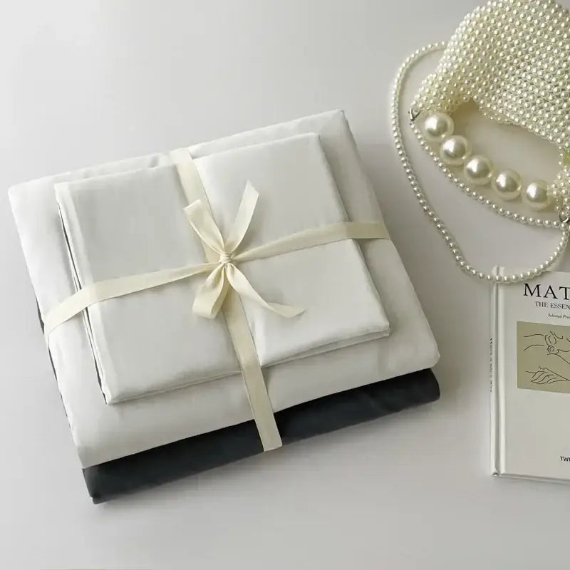 A neatly folded white satin pcs bed sheet set tied with cream ribbon from decorbites luxurious cotton bedding set