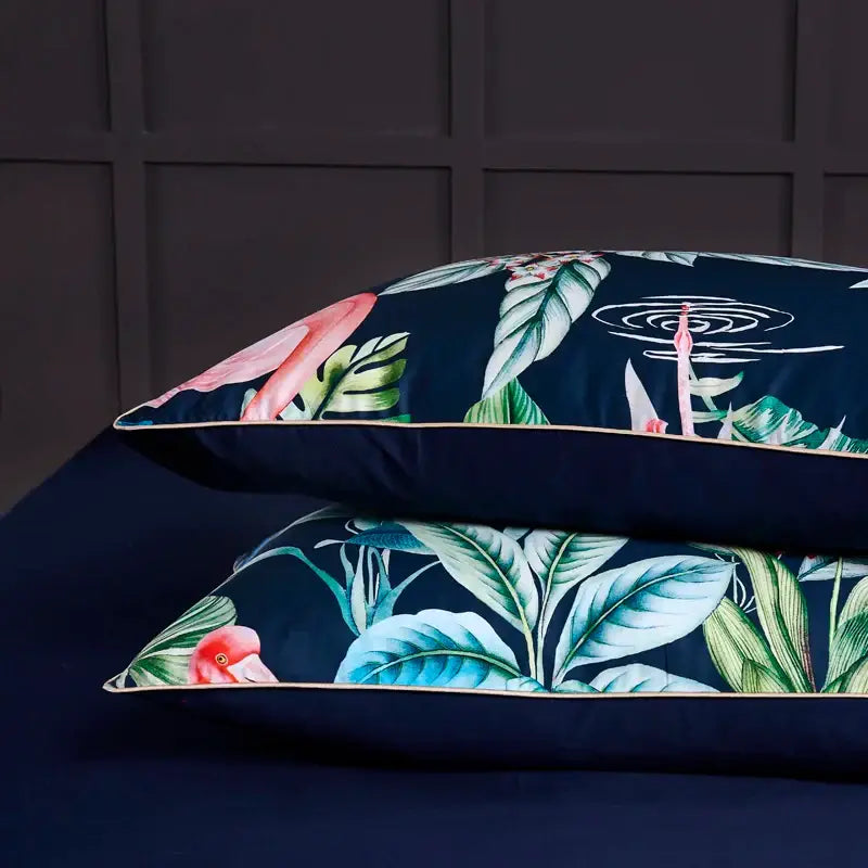 Dark blue pillowcases with vibrant pink flamingos and green foliage accented with gold piping in egyptian cotton pieces