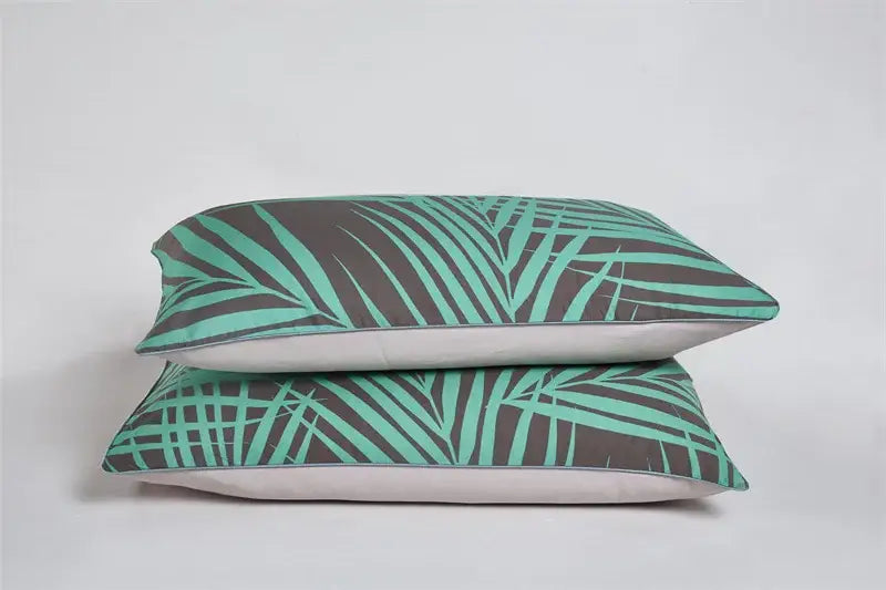 Two stacked rectangular pillows with teal and dark gray tropical leaf pattern and white linings from DecorBites™ egyptian cotton pillowcases