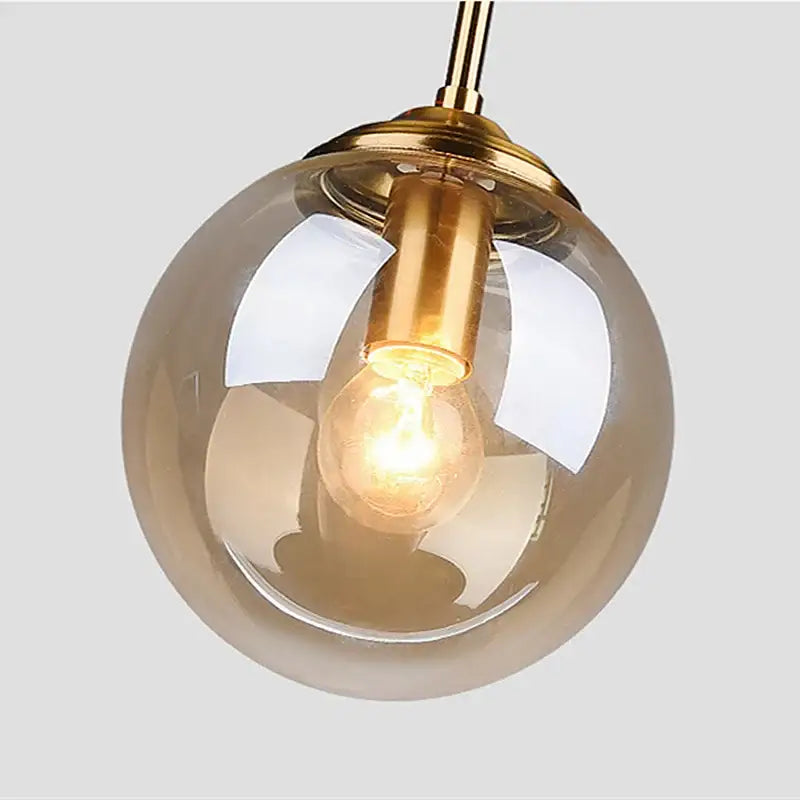 A warm-toned glass globe pendant light with brass finish and exposed filament bulb in luxury nordic led chandelier for dining room