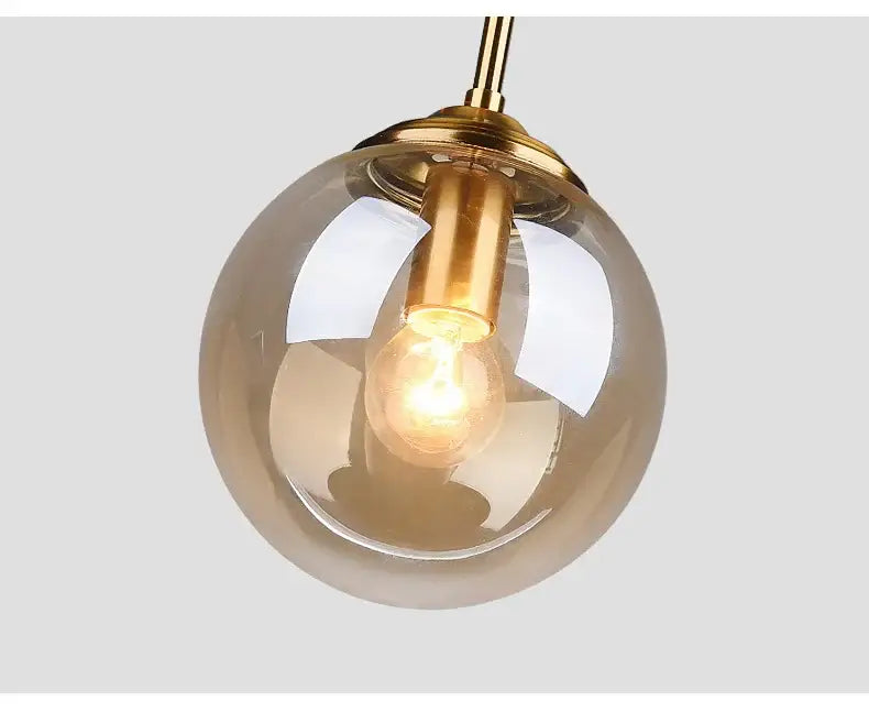 A warm-toned glass globe pendant light with brass fixture and exposed filament bulb in a luxury nordic led chandelier for dining room