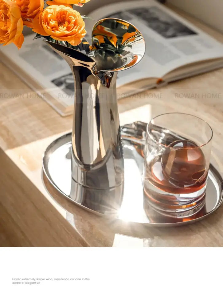 Shiny luxury stainless steel vase with flared trumpet-like opening holding orange roses for home decor