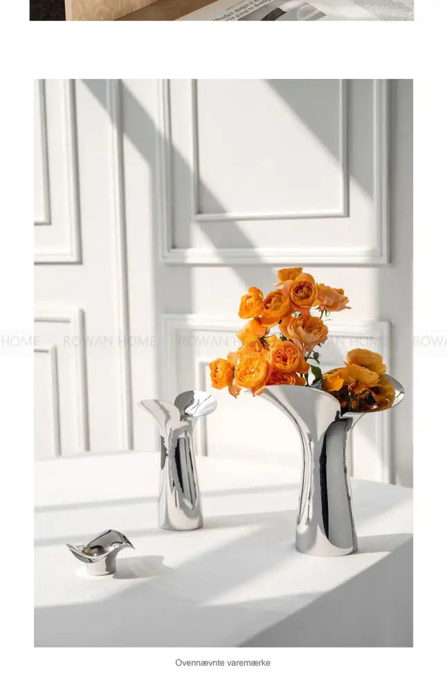 Shiny silver luxury stainless steel vase with sleek curved design holding vibrant orange roses for home decor