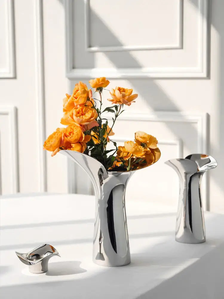 A sleek luxury stainless steel vase in silver holding vibrant orange roses for elegant home decor by decorbites