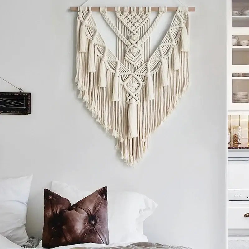 Cream-colored macrame wall hanging with intricate woven patterns and long fringe tassels for chic bohemian decor