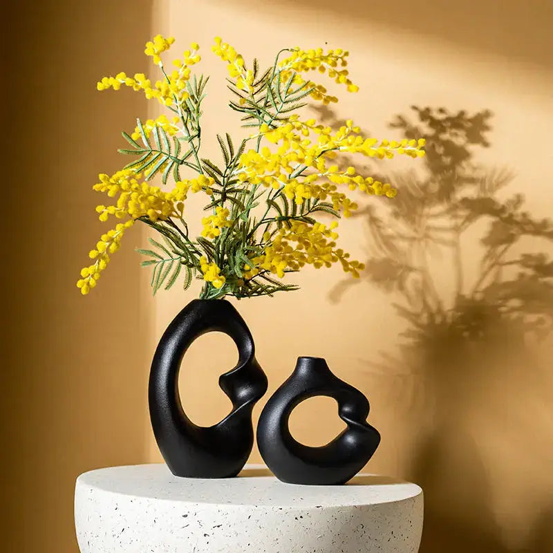 Two sleek black matte ceramic vases with abstract designs holding yellow mimosa flowers in a decorbites vase set for home decor