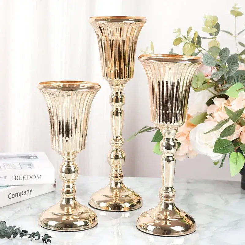 Three elegant gold metal trumpet vase candle holders with fluted ribbed designs and ornate stems for wedding decor