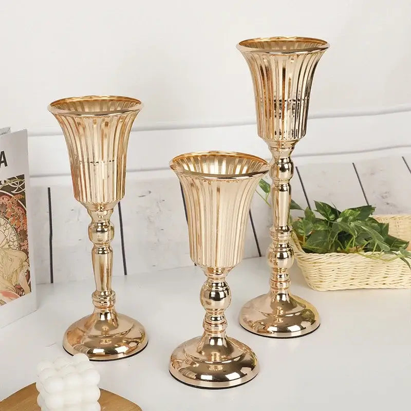 Three elegant gold metal trumpet vases with fluted ribbed designs and ornate bases for wedding centerpiece decor
