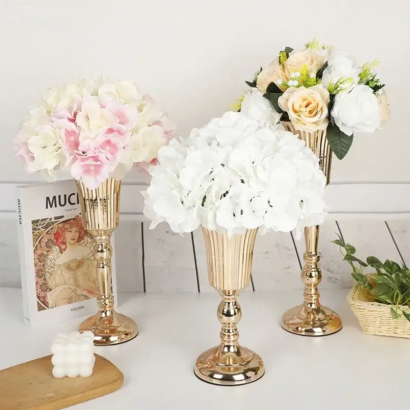 Three elegant gold-toned metal trumpet vases by DecorBites holding soft pink and white artificial flowers