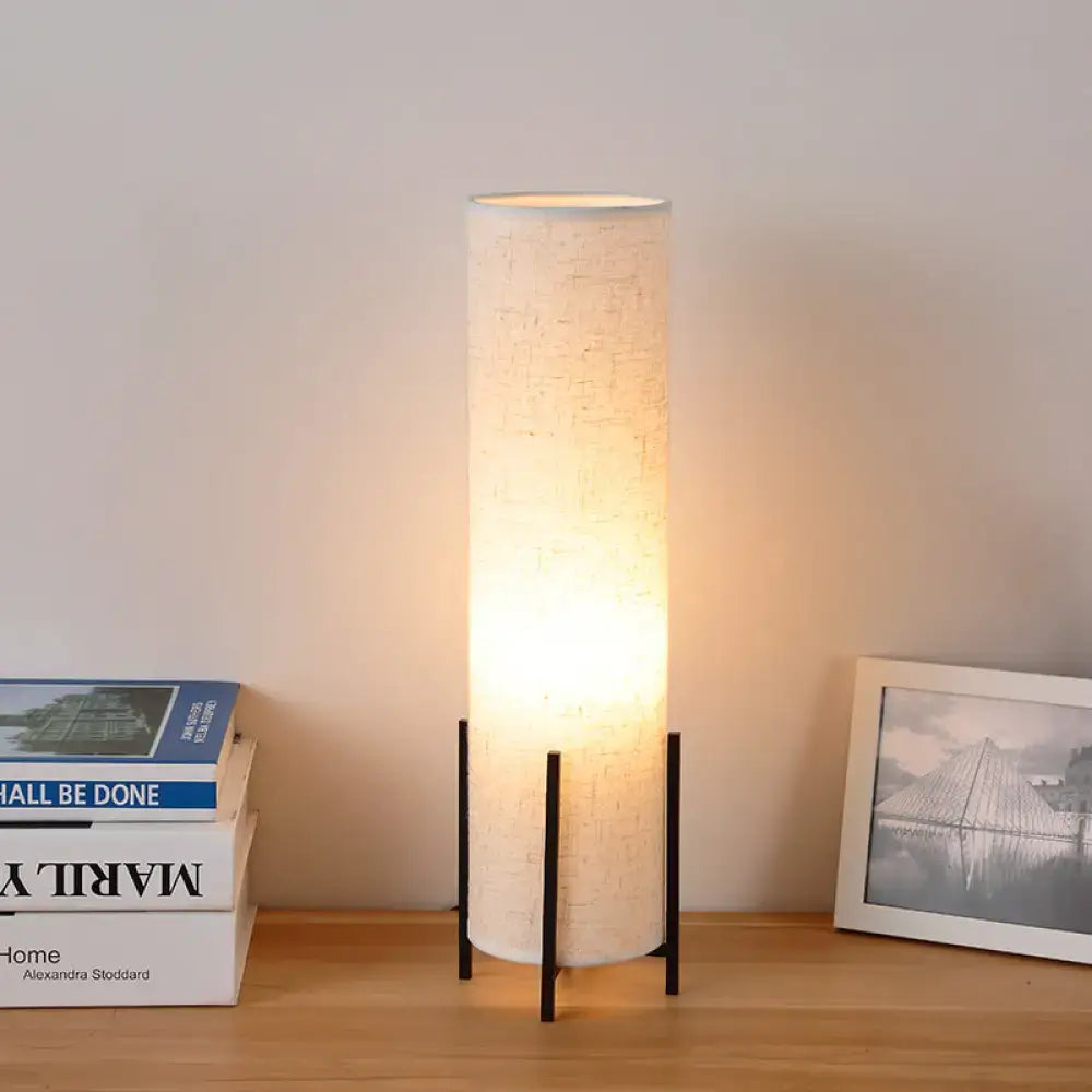 A beige minimalist tubular fabric nightstand floor lamp with black metal legs for reading by DecorBites