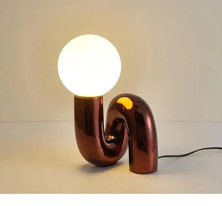 DecorBites™ modern art table lamp with a glossy copper curved base and glowing white spherical bulb for stylish lighting