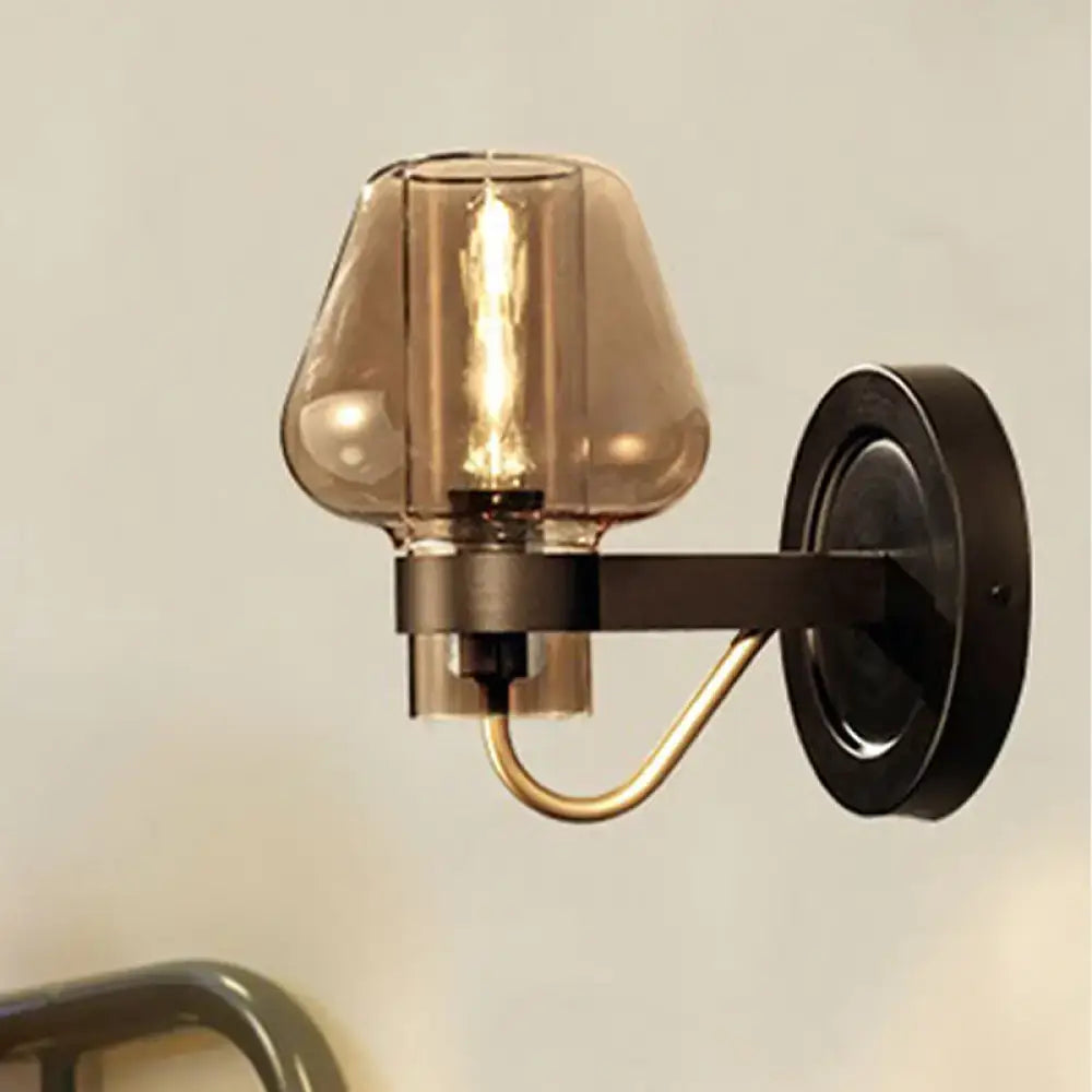 Modern black and brass wall sconce with amber glass shade and black metal arm for elegant bedroom lighting