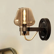 Modern black and brass wall sconce with amber glass shade and black metal arm for elegant bedroom lighting