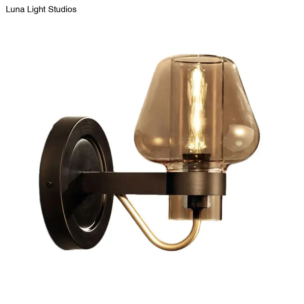 A modern black and brass wall sconce with a dark bronze base and amber glass shade for bedroom lighting