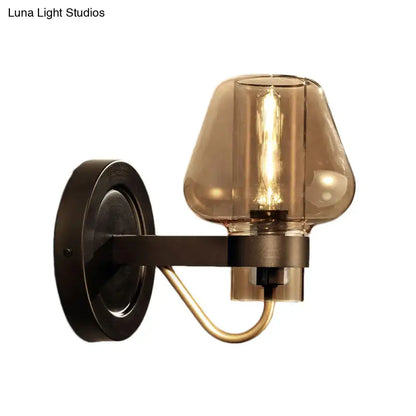 A modern black and brass wall sconce with a dark bronze base and amber glass shade for bedroom lighting