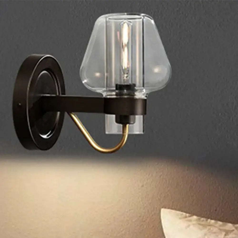 Modern black and brass wall sconce with a clear glass mushroom shade and exposed filament bulb for bedroom use