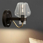 Modern black and brass wall sconce with a clear glass mushroom shade and exposed filament bulb for bedroom use