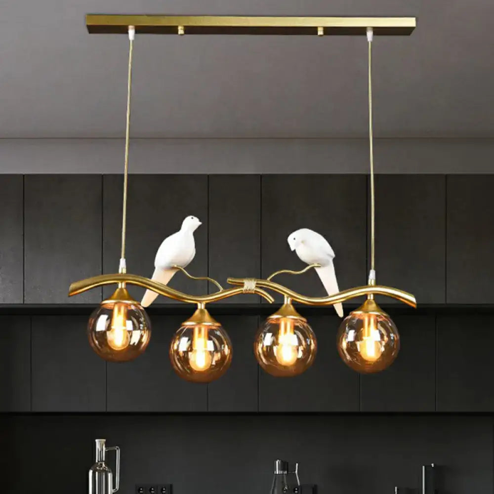Gold-toned metal island pendant light with curved branch design and white ceramic birds holding amber glass globe bulbs