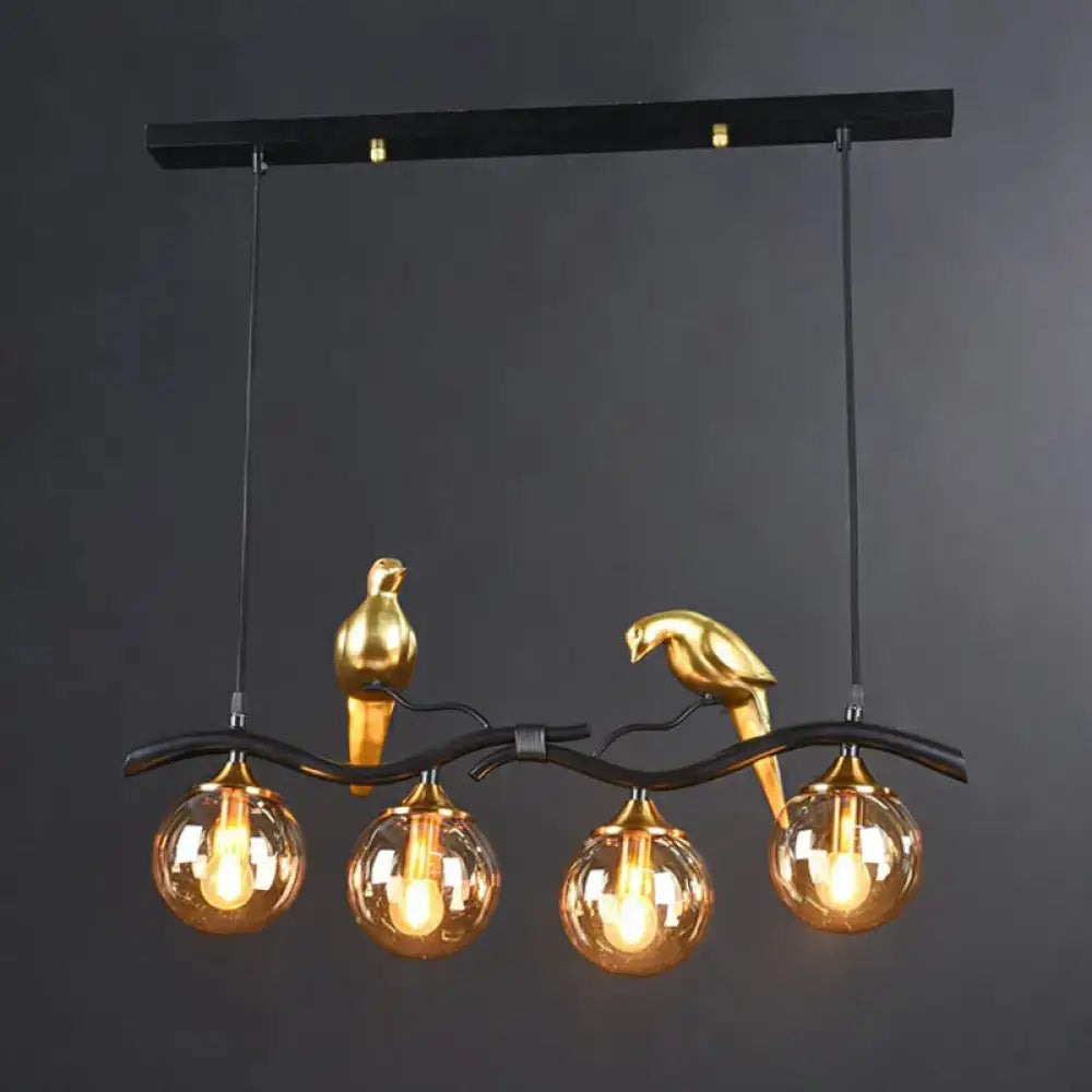 Gold-colored bird figurines perch on a black wrought iron branch holding amber glass globes in a decorbites island pendant light