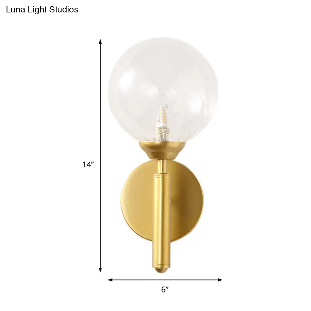 Modern brass wall lamp fixture with gold-toned cylindrical stem and clear glass globe for bedroom lighting