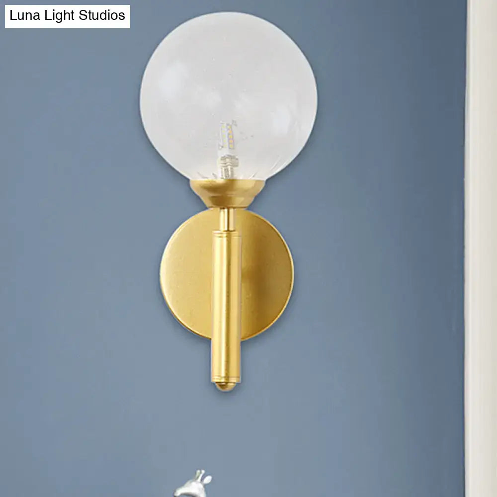 Gold-toned modern brass wall lamp fixture with frosted glass globe and sleek cylindrical stem for bedroom use