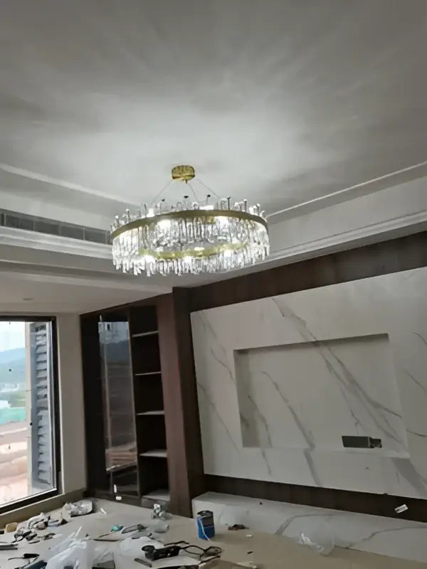 A gold-toned crystal chandelier with dangling droplets and circular frame for dining room by DecorBites™ golden chrome
