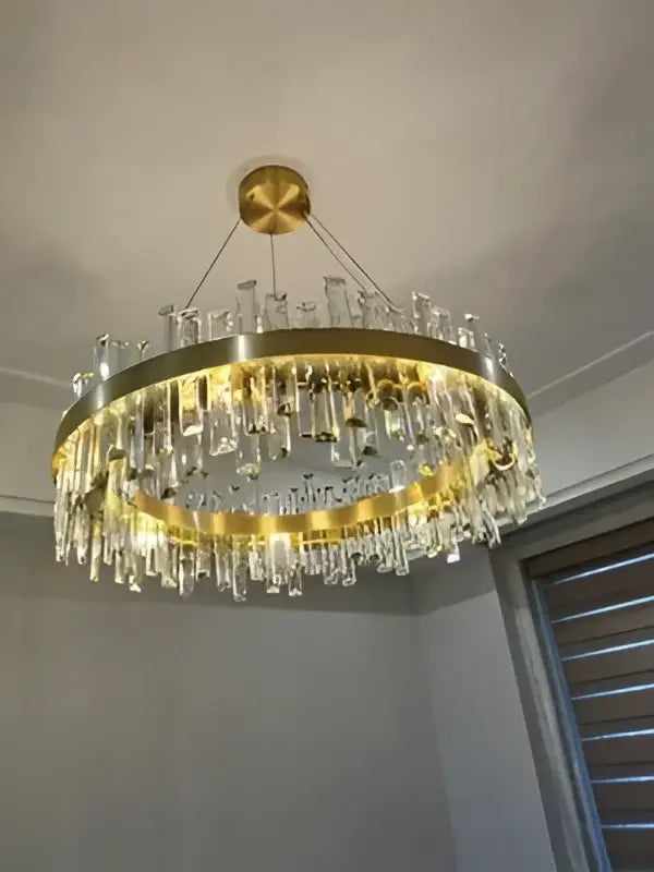 Gold-toned crystal chandelier with cascading clear prisms and circular brass frame for dining room lighting by DecorBites™