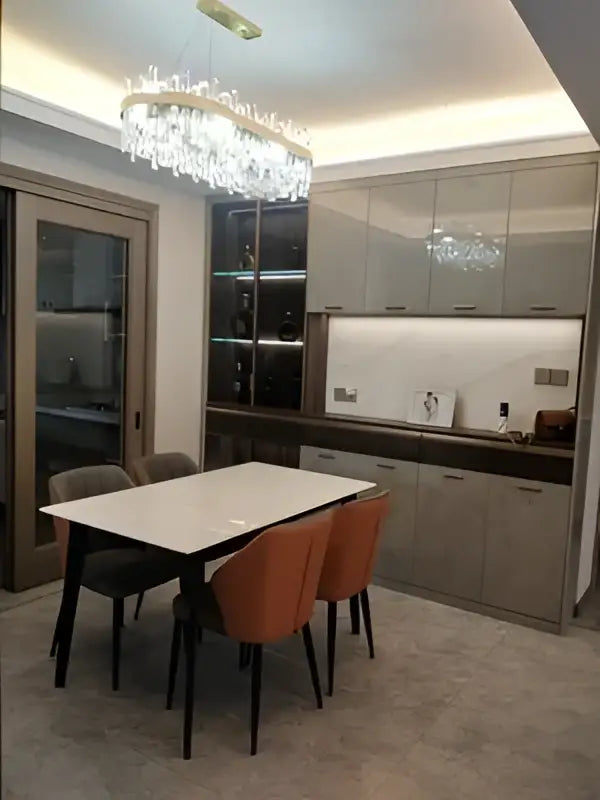 Modern dining room with a sleek white table black legs orange chairs and a decorbites crystal chandelier in golden chrome