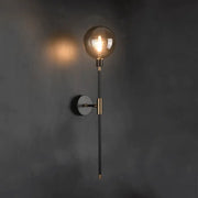 DecorBites™ modern glass wall sconce with spherical amber glass bulb and black metal stem accented by gold hardware
