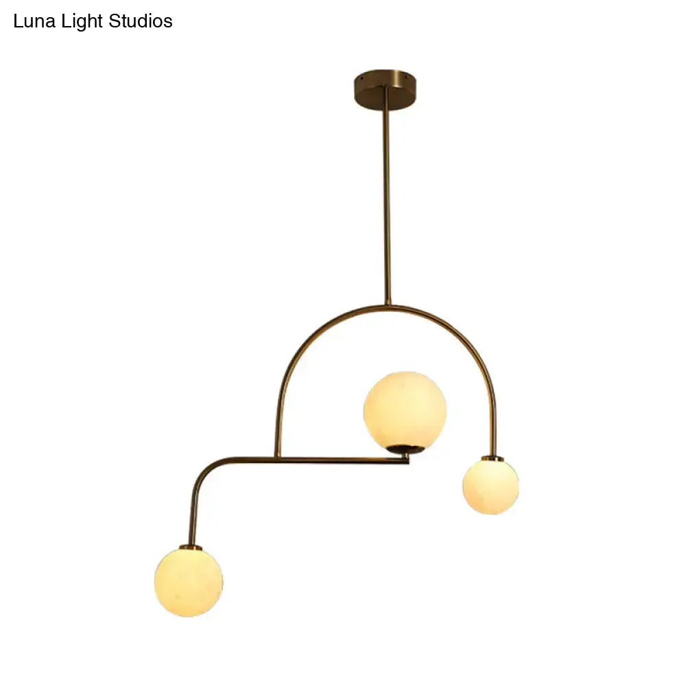 Brass-finished modern global bedroom pendant light with three yellow white frosted glass globe bulbs in an asymmetrical arc