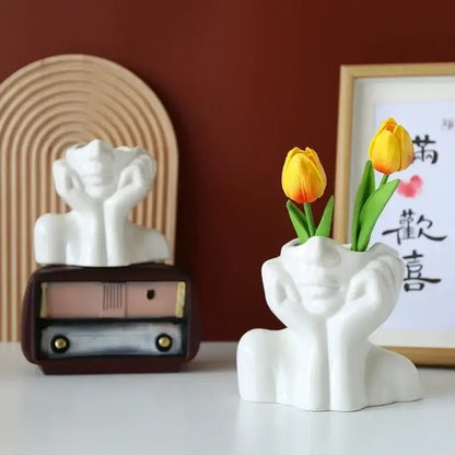 White ceramic DecorBites™ human body resin vase shaped with hands cupping face holding two yellow tulips