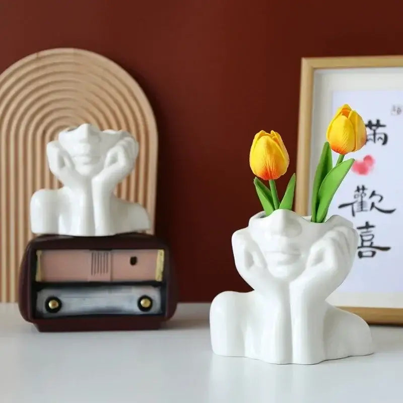 White ceramic DecorBites™ human body resin vase shaped with hands cupping face holding two yellow tulips