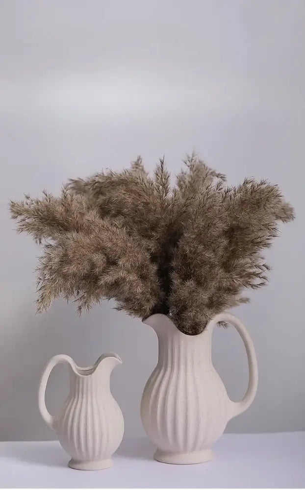 Cream-colored ins style ceramic spiral vase with vertical ribbed texture and curved handle filled with dried pampas grass