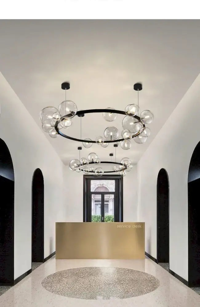 DecorBites™ modern black circular chandelier with clear glass bubble accents and adjustable cord above gold desk