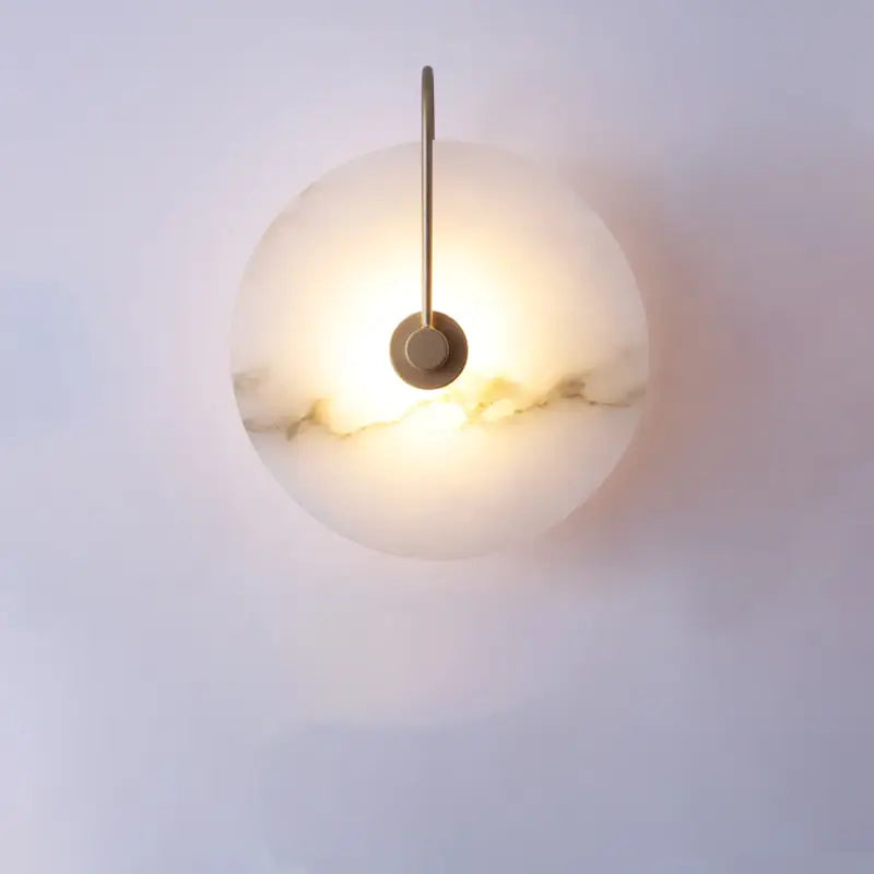 Decorbites modern marble wall lamp with warm glowing alabaster shade and slender brass finished arm on marble wall