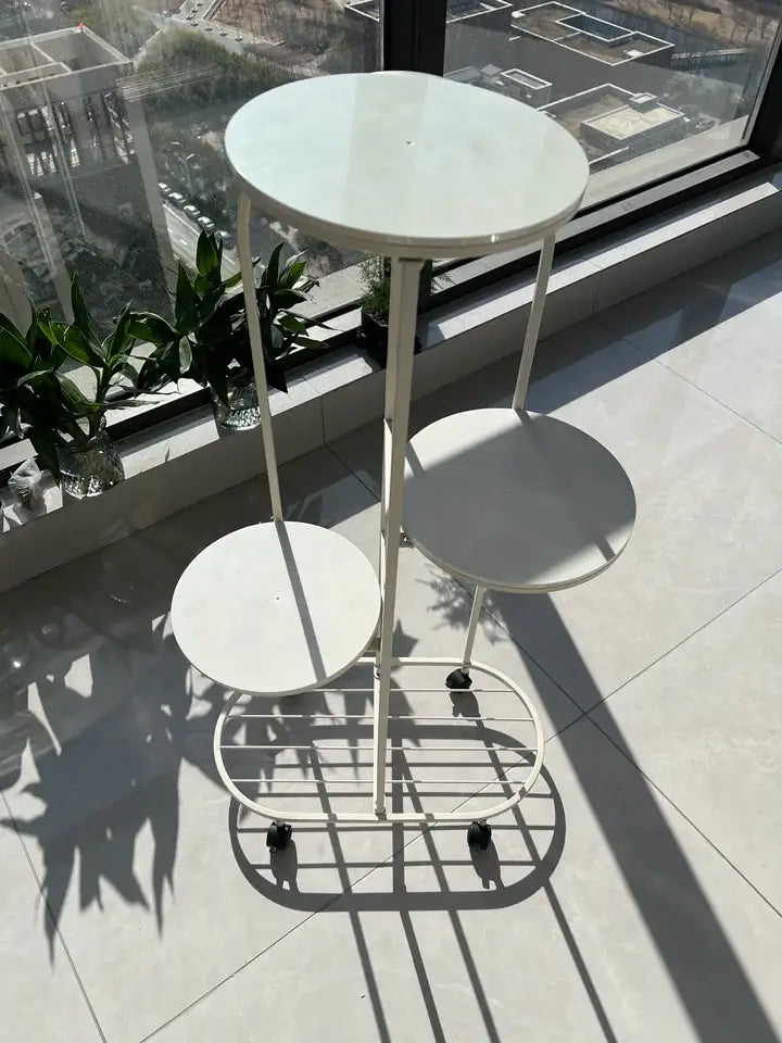 White metal tiered DecorBites™ plant stand with three circular shelves and black caster wheels for interior decor