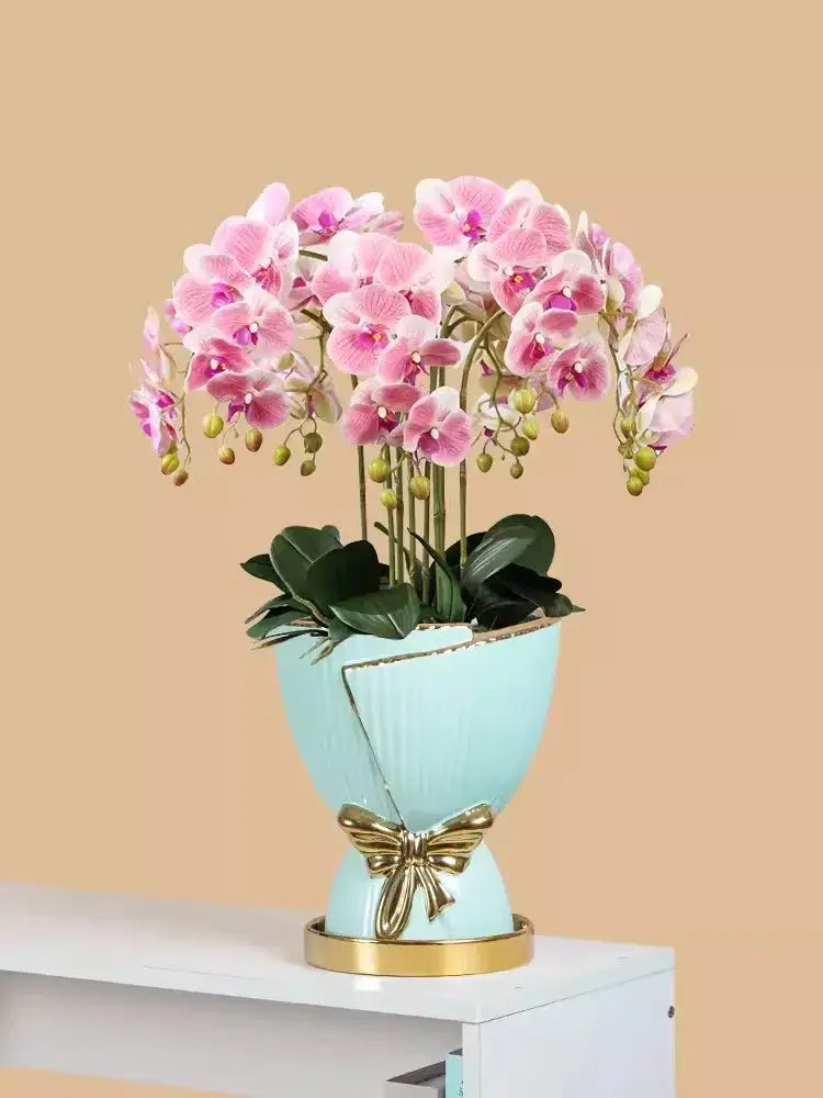 A light blue ceramic vase with gold bow and rim accents holding pink orchids for modern nordic home decor
